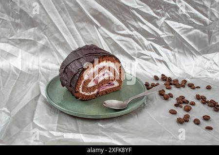 Schokoladenrolle mit Käse- und Waldfrüchtefüllung und Kaffeebohnen auf Keramikplatte, auf Silber Stockfoto