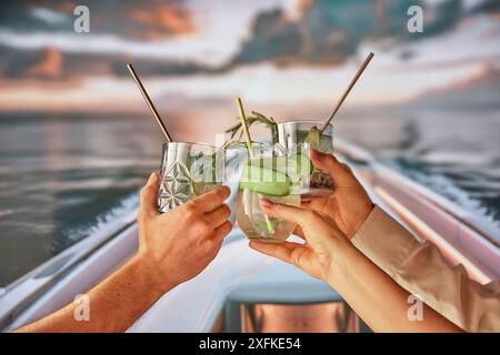 Gruppe von Menschen, Freunde, die sich am Abend auf der Yacht entspannen, die Hände an Gläsern mit Cocktails anschlagen, die ruhige Natur und den Sonnenuntergang genießen. Stockfoto