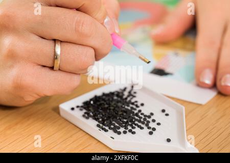 Eine Nahaufnahme einer Hand, die Kristalle auf einer Leinwand für ein Diamantmalprojekt platziert. Diamantmosaik Stockfoto
