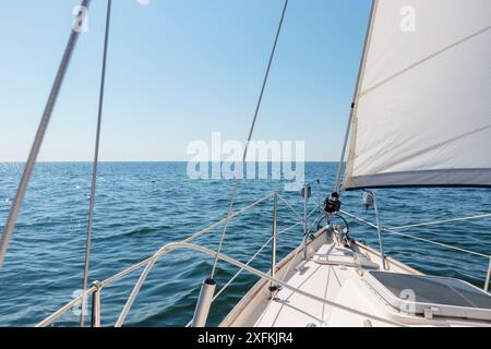 Weiße Sloop-Yacht, die bei Sonnenuntergang segelt. Klarer Himmel nach dem Sturm. Blick vom Deck zum Bug, Mast, Segeln. Transport, Reise, Kreuzfahrt, spo Stockfoto