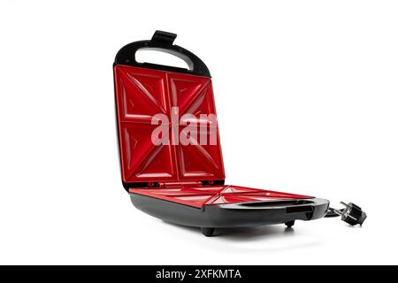 Ein roter und schwarzer elektrischer Sandwichmacher steht auf weißem Hintergrund. Der elektrische Sandwichmacher ist geöffnet und einsatzbereit. Stockfoto
