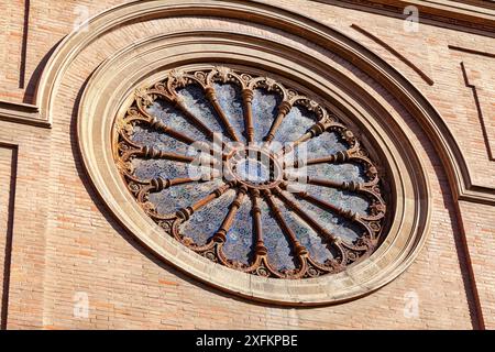 Buntglasfenster mit einem blauen Kreis in der Mitte. Das Fenster befindet sich auf einer Kathedrale mit einer Backsteinfassade Stockfoto