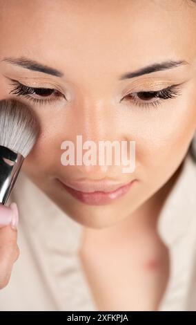 Ein Maskenbildner trägt Puder auf das Gesicht eines weiblichen Models auf. Professionelles Make-up-Konzept Stockfoto