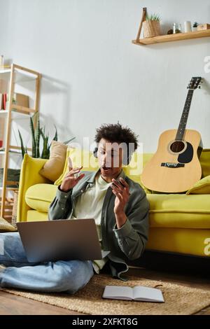 Junger Mann, der online Musik mit Gitarre und Laptop kreiert. Stockfoto