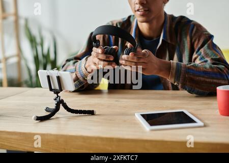 Junger afroamerikanischer männlicher Blogger mit Kopfhörern, der ein Tablet am Tisch benutzt. Stockfoto