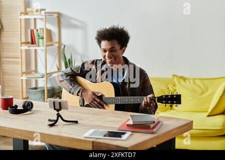 Ein junger Mann stampft seine Akustikgitarre in einem gemütlichen Wohnzimmer. Stockfoto