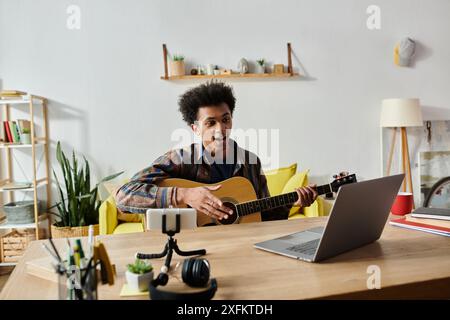 Ein junger Mann spielt Akustikgitarre vor einem Telefon und nimmt für seinen Blog auf. Stockfoto