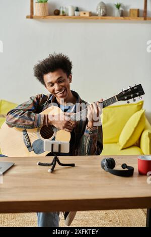 Ein Mann schnappt eine Akustikgitarre vor ein Telefon, um Musik für ein Online-Publikum zu kreieren. Stockfoto