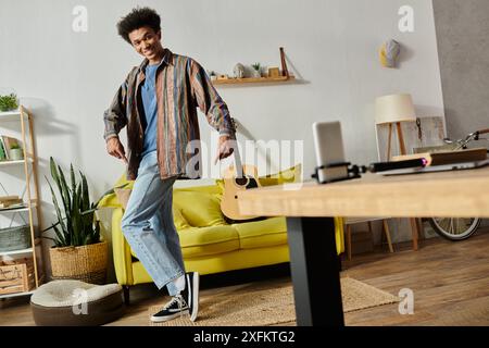 Junger afroamerikanischer Blogger, der Gitarre spielt, mit der Telefonkamera vor der gelben Couch spricht. Stockfoto