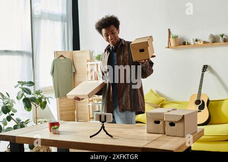 Junger afroamerikanischer Mann mit Pappkarton beim Vloggen im Wohnzimmer. Stockfoto