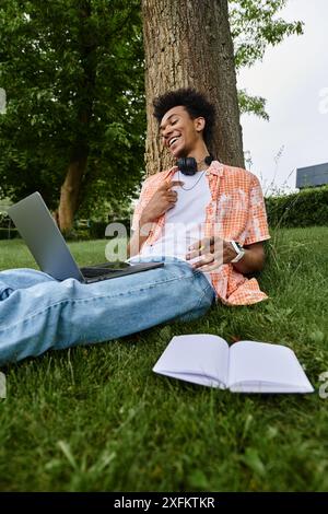 Der junge Mann genießt Musik und arbeitet auf dem Laptop im Gras. Stockfoto