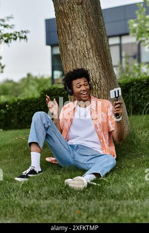 Ein junger Mann afrikanischer Herkunft sitzt auf Gras neben einem Baum. Stockfoto