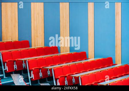 Eine Weitwinkelaufnahme eines modernen Auditoriums mit Reihen roter Sitze und Holzpaneelen an der Wand. Die Sitze sind in einer Stufenform angeordnet Stockfoto