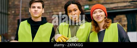 Drei umweltbewusste junge Freiwillige in Handschuhen und Sicherheitswesten stehen nebeneinander und sortieren gemeinsam Müll. Stockfoto