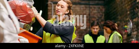 Eine junge Frau in einer gelben Weste nimmt weggeworfene Gegenstände auf, während sie sich freiwillig mit anderen umweltbewussten Personen zusammensetzt. Stockfoto