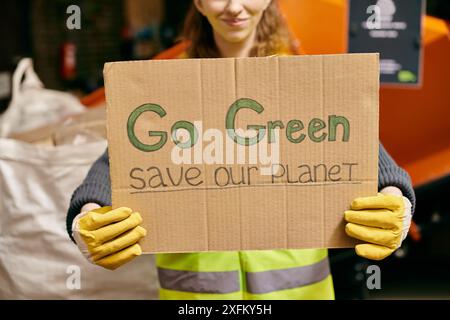 Ein junger Freiwilliger in Handschuhen und Sicherheitsweste hält ein Schild mit der Aufschrift „Go Green Rettet unseren Planeten“ in einem leidenschaftlichen Aufruf zur Aktion. Stockfoto