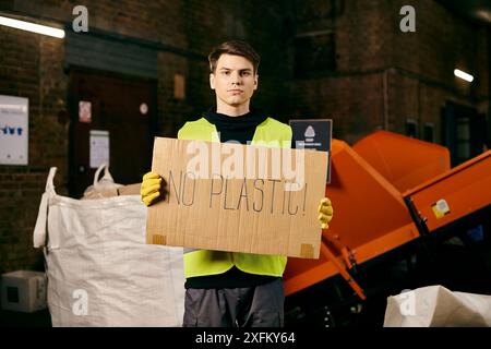 Junge Freiwillige in Handschuhen und Sicherheitsweste setzen sich gegen Plastikverschmutzung ein, indem sie ein Schild mit der Aufschrift „kein Plastik“ halten. Stockfoto