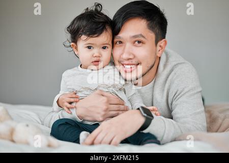 Asiatische Familie, Vater und Baby im Porträt auf dem Bett, Verbundenheit und Kinderbetreuung mit Alleinerziehenden zu Hause. Schlafzimmer, kleines Mädchen und stolzer Vater Stockfoto