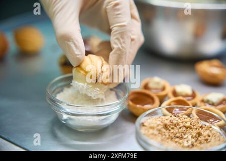 Bäckerin taucht süße Konditornüsse in weiße Schokolade in Kokosflocken Stockfoto