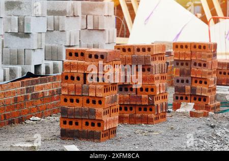 Rote Steine und Betonblöcke, die auf der Baustelle geliefert und neben dem Arbeitsort für Maurer aufgestellt wurden Stockfoto