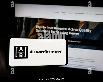 Person mit Smartphone und Logo der US-Investmentgesellschaft AllianceBernstein Holding L.P. (ab) vor der Website. Schwerpunkt auf dem Display des Telefons. Stockfoto