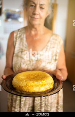 Eine ältere Frau präsentiert eine frisch zubereitete spanische Tortilla auf einem Teller und zeigt hausgemachte Küche. Stockfoto