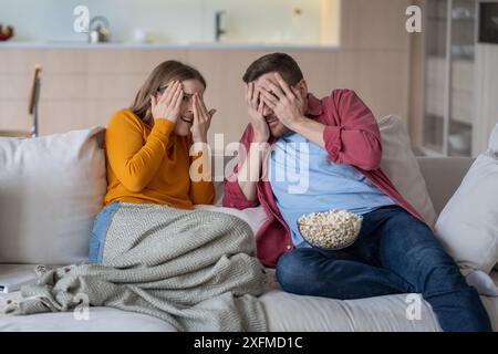Ängstliches verheiratetes Paar, Ehemann Frau sitzt auf der Couch und hat Angst vor Horrorfilm im Fernsehen Stockfoto