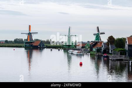 Eine Gruppe von Windmühlen befindet sich auf einem See mit einer roten Boje im Wasser. Die Windmühlen sind grün und weiß und befinden sich in der Nähe eines Dorfes Stockfoto