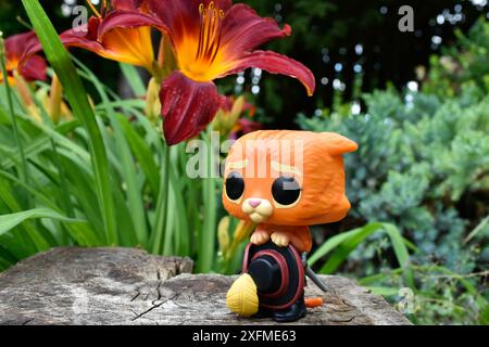 Funko Pop Actionfigur von Puss in Stiefeln mit gefiedertem Hut aus dem Zeichentrickfilm Shrek. Märchenwald, Baumstumpf, orange Blumen, fabelhafter Charakter. Stockfoto