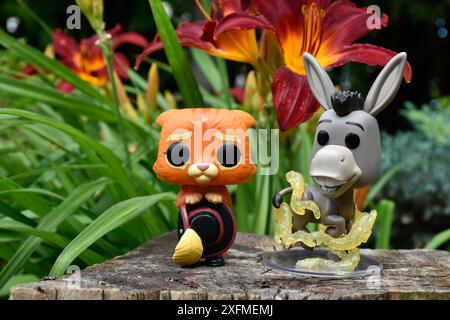 Funko Pop Actionfiguren von Esel und Puss in Stiefeln aus dem beliebten Zeichentrickfilm Shrek. Märchenwald, Baumstumpf, orange Blumen, fabelhafte Charaktere. Stockfoto