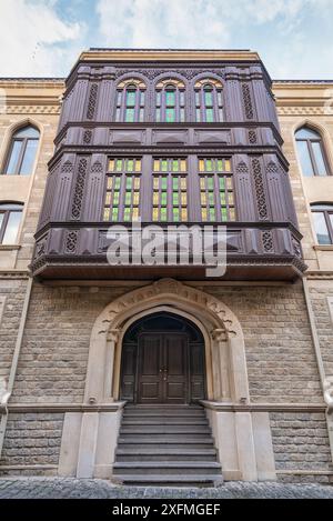 Ein traditionelles aserbaidschanisches Gebäude in der Altstadt von Baku, alias Icherisheher, verfügt über einen kunstvollen Holzbalkon mit Buntglasfenstern und einen großen Eingang mit einer Treppe Stockfoto