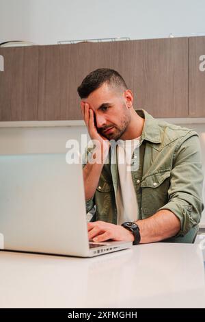 Vertikal. Hart arbeitender Mann, verzweifelt wegen Laptop-Problemen, die ihr Stress und Kopfschmerzen verursachen. Ein frustrierter Burnout-Typ, der mit übermäßiger Arbeit zu tun hat Stockfoto