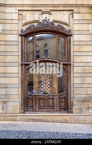 Eine Schaufensterfront mit einem kunstvollen Holzfenster, auf dem ein gemusterter Teppich in der Altstadt, alias Icherisheher, in Baku, Aserbaidschan, zu sehen ist Stockfoto