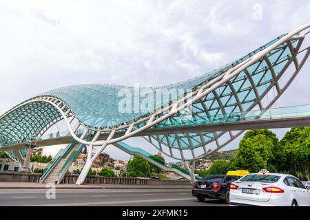 Tiflis, Georgien – 17. Juni 2024: Die Friedensbrücke ist eine bogenförmige Fußgängerbrücke, eine Stahl-Glas-Konstruktion über den Fluss Kura, die die Brücke verbindet Stockfoto