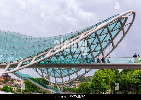 Tiflis, Georgien – 17. Juni 2024: Die Friedensbrücke ist eine bogenförmige Fußgängerbrücke, eine Stahl-Glas-Konstruktion über den Fluss Kura, die die Brücke verbindet Stockfoto