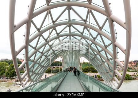 Tiflis, Georgien – 17. Juni 2024: Die Friedensbrücke ist eine bogenförmige Fußgängerbrücke, eine Stahl-Glas-Konstruktion über den Fluss Kura, die die Brücke verbindet Stockfoto