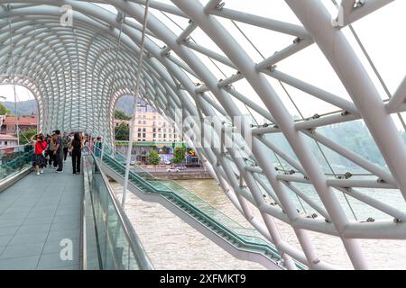 Tiflis, Georgien – 17. Juni 2024: Die Friedensbrücke ist eine bogenförmige Fußgängerbrücke, eine Stahl-Glas-Konstruktion über den Fluss Kura, die die Brücke verbindet Stockfoto