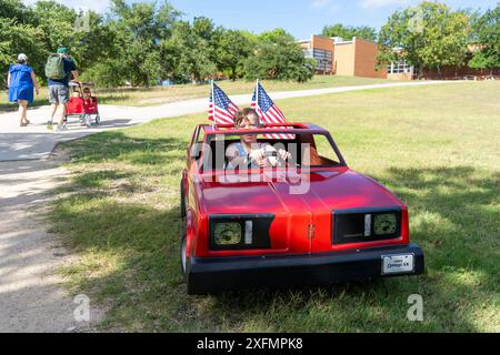 Austin, Texas, USA, 4. Juli 2024. Während der jährlichen Parade am 4. Juli in Barton Hills sitzt ein Junge in einem Spielzeugauto mit fliegenden amerikanischen Fahnen auf dem Spielplatz der Barton Hills Elementary School. Ein paar hundert Einwohner gingen auf der 1/2 km langen Paradestraße zum Schulgelände, wo sie Kekse, Wassermelonen und Eis genossen. Quelle: Bob Daemmrich/Alamy Live News Stockfoto