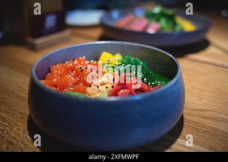 Eine lebendige Poke-Schüssel mit frischem Lachs, Algen, Avocado und Sesamsamen auf einem Holztisch Stockfoto
