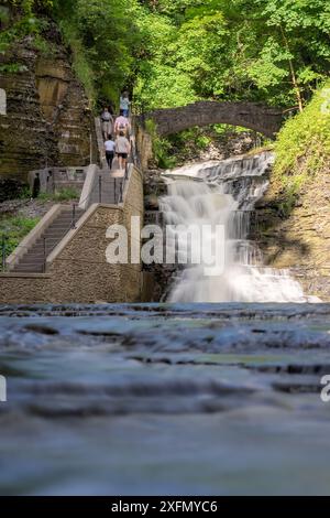 Vertikales Foto eines Wasserfalls mit einem Pfad / Betontreppe, Cascadilla Gorge Trail, in Ithaca, NY, USA. Stockfoto