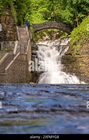 Vertikales Foto eines Wasserfalls mit einem Pfad / Betontreppe, Cascadilla Gorge Trail, in Ithaca, NY, USA. Stockfoto