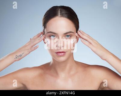 Frau, Porträt und Creme zum Leuchten im Studio, Feuchtigkeit und glatte Schönheit auf blauem Hintergrund. Weibliche Person, Anwendung und Gesichtslotion Stockfoto