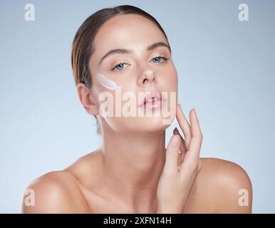 Frau, Porträt und Creme für klare Haut im Studio Porträt, Feuchtigkeit und Schönheit auf blauem Hintergrund. Person, Anwendung und Gesichtslotion Stockfoto