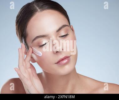 Frau, Kosmetik und Creme für klare Haut im Studio, Feuchtigkeit und Schönheit auf blauem Hintergrund. Weibliche Person, Anwendung und Gesichtslotion Stockfoto