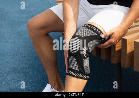 Mann, der eine Kniestracke zur Unterstützung eines schmerzhaften Beins einlegt. Bodybuilder-Bein des Athleten mit Kniestraße oder elastischer Kniescheibenbandage. Hülse für Kompression. Stockfoto