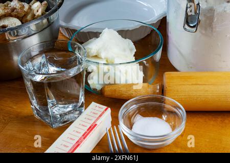 Zutaten für einen Kuchen, einschließlich: Schüssel mit Füllung, Butter, Salz, Wasser, Kürzen, und Mehl für die Kruste. Zu den Utensilien gehören eine Gabel, ein Tortenplatte und Stockfoto