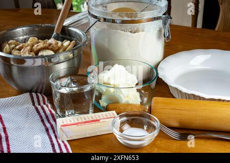 Zutaten für einen Kuchen, einschließlich: Schüssel mit Füllung, Butter, Salz, Wasser, Kürzen, und Mehl für die Kruste. Zu den Utensilien gehören eine Gabel, ein Tortenplatte und Stockfoto