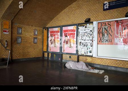 Obdachloser, spärlich bekleidet und barfuß, schläft auf seinem kargen Lager, bestehend aus zwei Decken auf dem kalten Fliesenboden - Berlin, Deutschland, Deutschland, Deutschland, 26.06.2024 - Berlin-Mitte Ortsteil Wedding: Die Lagerstätte des Obdachlosen befindet sich am Eingang einer S-Bahnstation. Die angrenzenden Straßen sind zu einem Anlaufpunkt für die Alkohol- und Drogenszene geworden, insbesondere trifft sich hier seit geraumer Zeit die Crack-Szene. Immer mehr Menschen leben in Berlin ohne festen Wohnsitz auf der Straße. *** Obdachloser, spärlich bekleidet und barfuß, schläft in seinem dürftigen Lager, Betrüger Stockfoto