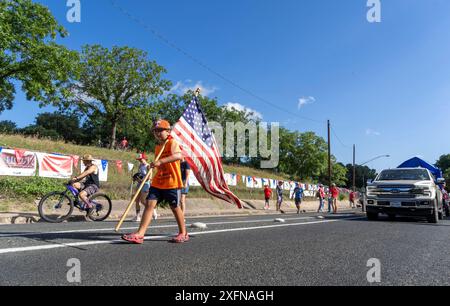 Austin, Tx, USA. Juli 2024. Ein Junge mit einer großen amerikanischen Flagge spaziert am 4. Juli 2024 auf dem Barton Hills Drive während der jährlichen Parade in der Nachbarschaft Barton Hills in Süd-Austin, Texas. Einige hundert Einwohner gingen zu Fuß auf die 1/2 km lange Parade zur Grundschule und genossen Kekse, Wassermelonen und Eis. (Kreditbild: © Bob Daemmrich/ZUMA Press Wire) NUR REDAKTIONELLE VERWENDUNG! Nicht für kommerzielle ZWECKE! Stockfoto