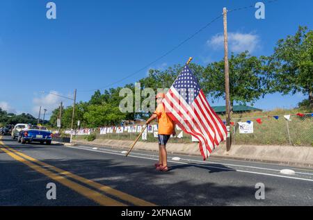 Austin, Tx, USA. Juli 2024. Ein Junge mit einer großen amerikanischen Flagge spaziert am 4. Juli 2024 auf dem Barton Hills Drive während der jährlichen Parade in der Nachbarschaft Barton Hills in Süd-Austin, Texas. Einige hundert Einwohner gingen zu Fuß auf die 1/2 km lange Parade zur Grundschule und genossen Kekse, Wassermelonen und Eis. (Kreditbild: © Bob Daemmrich/ZUMA Press Wire) NUR REDAKTIONELLE VERWENDUNG! Nicht für kommerzielle ZWECKE! Stockfoto